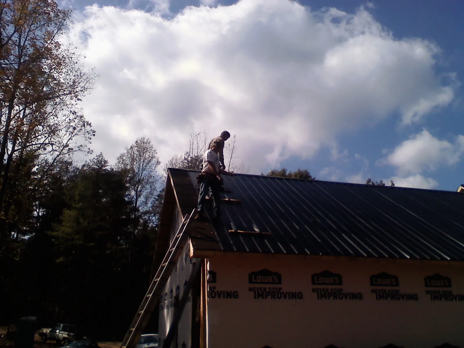 Roofer fastening dark metal panels high against a cloudy sky, from a Roof Inspection job in Parkersburg