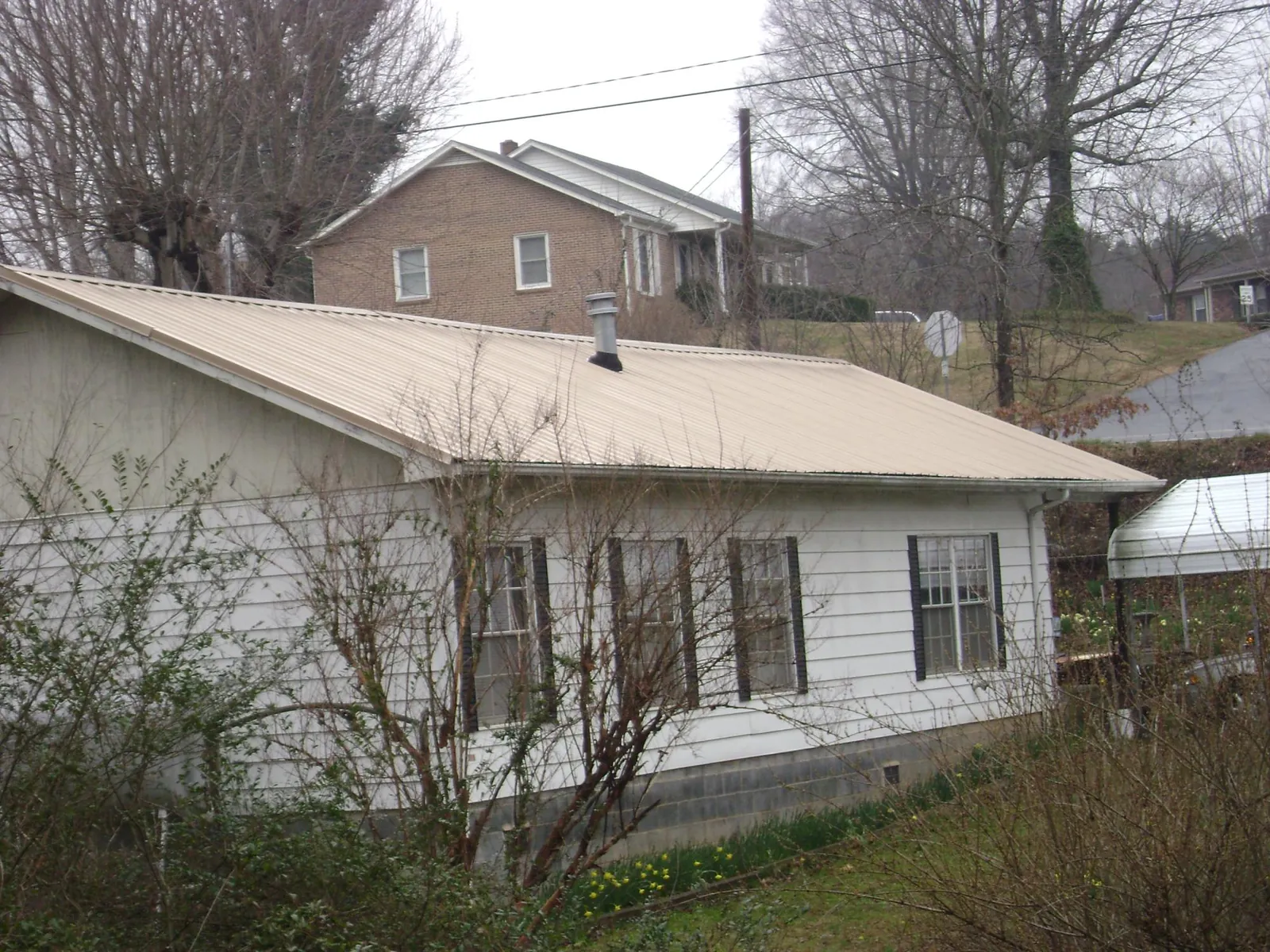 Tan metal roof on a white sided house set into a hillside in Parkersburg